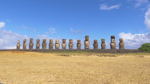 AERIAL: Mysterious monoliths with human faces in Chile all facing the same direction. Breathtaking shot of a row of famous moai statues under the clear blue summer sky on a remote volcanic island.