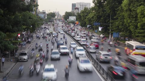 HANOI / VIETNAM - JULY 25, 2018: Time lapse of a big road with busy traffic during rush hour. Cars, motorbikes, buses, taxis commuting at the end of the day.