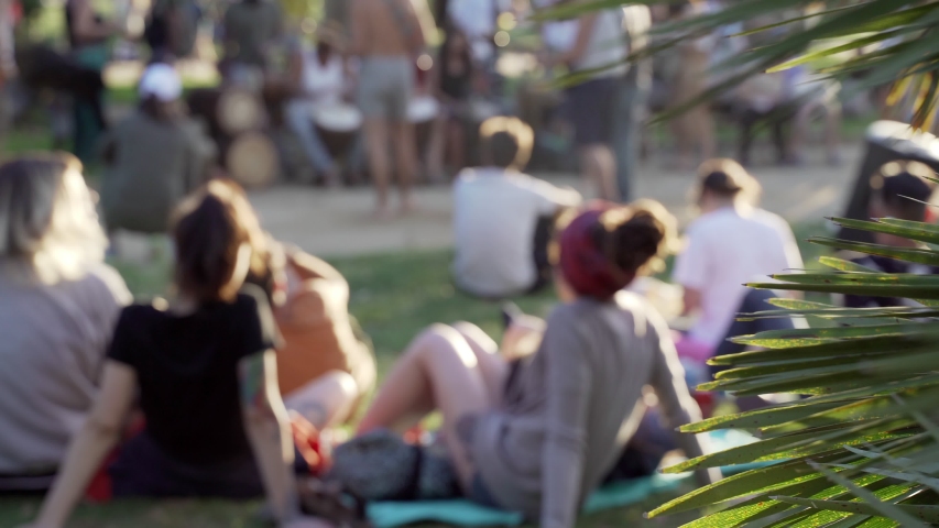 Park in the city. Different activities in the urban park, people sitting on the green grass, chilling, listening to the music, drinking beer with friends. Summertime in Barcelona. Golden light 
