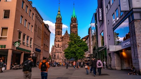 NUREMBERG, GERMANY - CIRCA MAY 2019: Time-lapse view on daily life as people pass by in the old town with the famous church St. Lawrence in the background circa May 2019 in Nuremberg, Germany.
