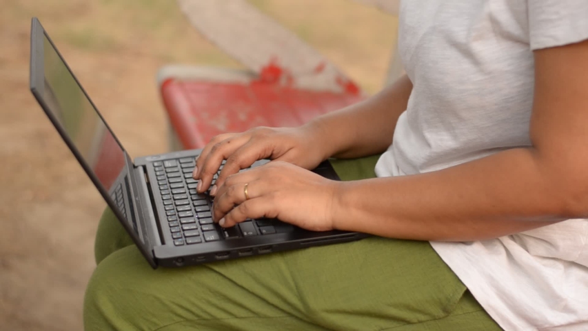 Young Indian woman working on a laptop sitting on a red bench in a park in New Delhi, India