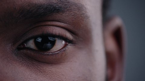 Highly detailed portrait of young mature man staring at camera. Close-up cropped view of beautiful african black man eye on grey background.