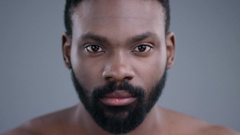 Portrait of sensual handsome african man with confident expression. Close-up of appealing black male model looking at camera on grey background.