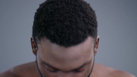Close-up of beautiful african man face looking at camera on grey background. Portrait of handsome shirtless male model with beard.