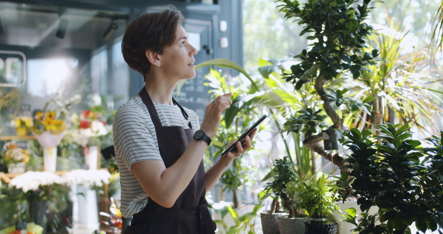 Young entrepreneur touching tablet screen looking at flowers in florist's shop enjoying nature and modern technology. People, entrepreneurship and business concept. Royalty-Free Stock Footage #1031741117