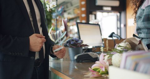 Guy customer is giving cash money to cashier then taking flowers from florist purchasing gift in floral shop. Business, finance and consumerism concept.
