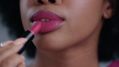 Close-up view of sexy beautiful african girl rouging her lips with mouth opened. Lovely black woman applying pink lipstick on her lips and giving an air kiss on camera.