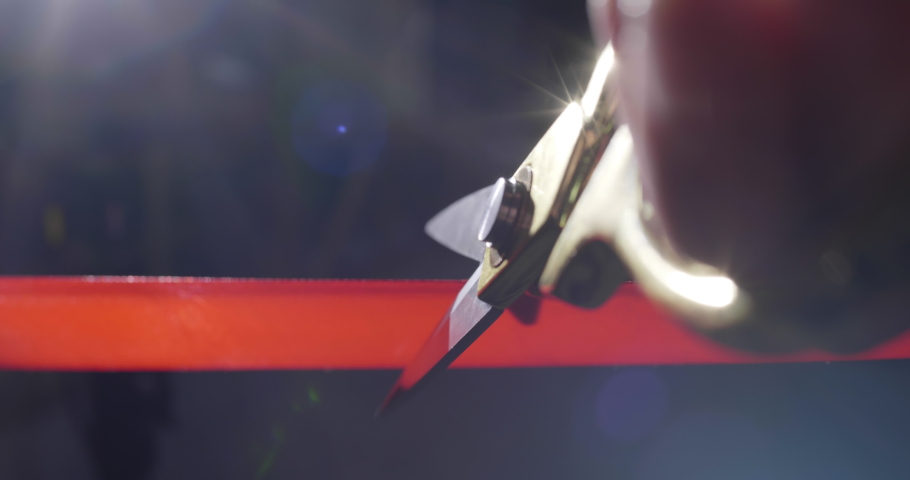 Closeup of a man's hand cutting a red ribbon with shiny scissors