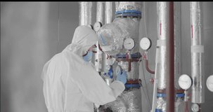 heating engineer in protective coverall and mask in boiler room taking readouts or adjusting meter - Powered by Shutterstock - Get 15% off with code: PIKWIZARD15