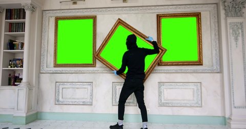 Portrait of robber putting on balaclava stealing painting from art gallery. Green screen, slow motion, chromakey