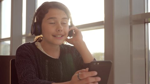 Happy young teenage girl in headphones sings and listening to the music on smartphone. teenager lifestyle girl in social networks listens to music sitting in a cafe