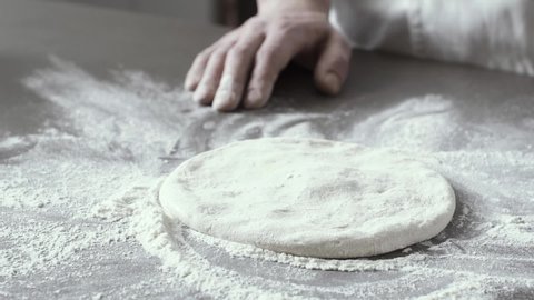 Professional pizza maker stretching and dusting the dough with flour on the kitchen worktop