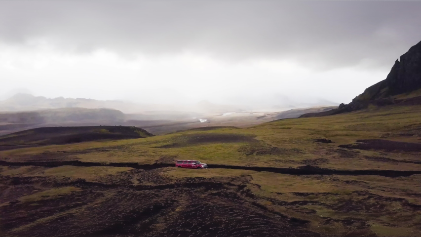 Drone aerial shot of res super jeep driving on gravel road with mouintains in the background in Iceland