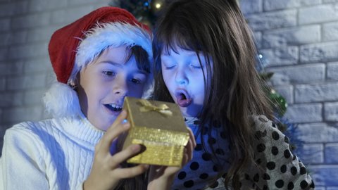 Magic Christmas present. Two girls admire a gold present box, shake it and with surprise open it. The box glows blue.