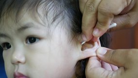 A mother's hands using a cotton swab to clean her little Asian baby girl's ear canals - cleaning inside children's ears could cause a wax buildup in the first place