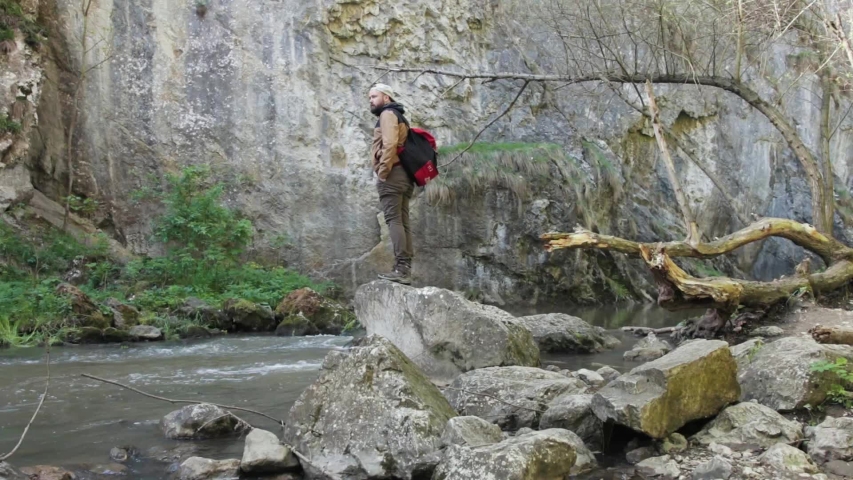 Mountaineer standing on a huge rock next to an amazing mountain river.