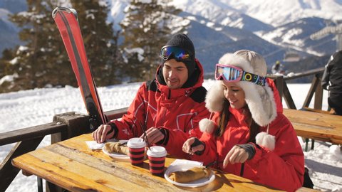 Couple of skiers on the mountain having lunch in restaurant outdoors.