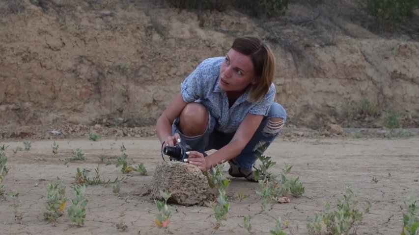 A middle-aged woman in a squatting shirt makes a photo with a small camera.