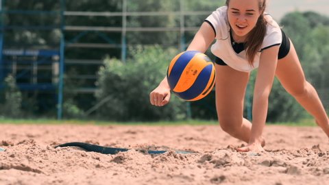 Young female athlete dives into the sand and saves a point during beach volleyball match. Cheerful Caucasian girl jumps and crashes into the white sand during a beach volley tournament