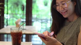 Young asian woman using smartphone and drinking iced coffee with stainless straw, eco friendly lifestyle