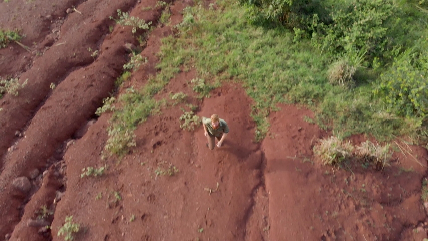 Aerial birds eye view of a bearded ginger outdoors man as he walks up a mountain.