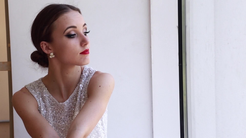 Young tired woman ballet dancer sitting on a windowsill near a big window in a studio.