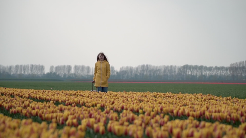 Young teenage girl walking through yellow tulip field in a yellow rain coat