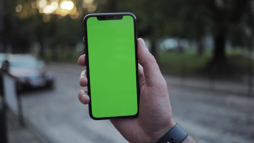 Busy young man holding mockup smartphone touching and swiping on green screen surfing social networks outdoors on the street. | Shutterstock HD Video #1031820182