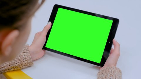 Woman sitting at table and looking at black digital tablet computer device with blank green screen in cafe. Technology, chroma key, template, mockup and entertainment concept
