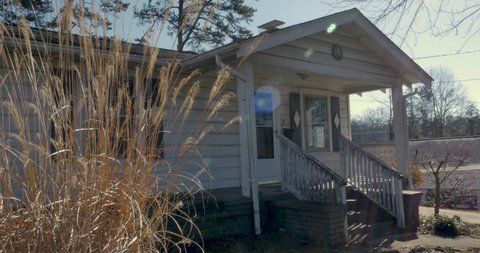Establishing shot of a small one story house with tall dead grass in the foreground - dolly shot