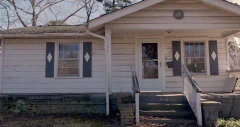 Front entrance of a one story rundown empty single family home during the winter - dolly establishing shot