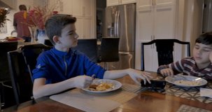 Two young brothers passing a mobile phone back and forth while eating scrambled eggs and sausage for breakfast