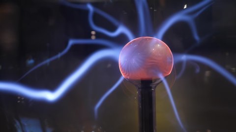Blue filaments of electric energy flows from central electrode of plasma sphere, lively and changing streams move around, red glow on ball surface
