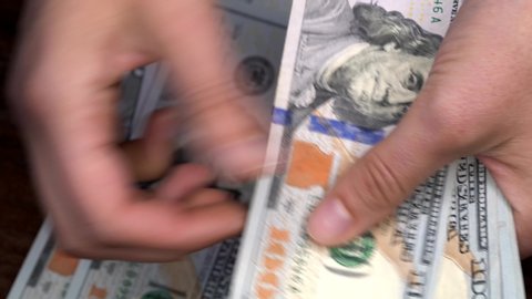 This close up video shows an anonymous pair of caucasian hands counting money from a new stack of hundred dollar bills.