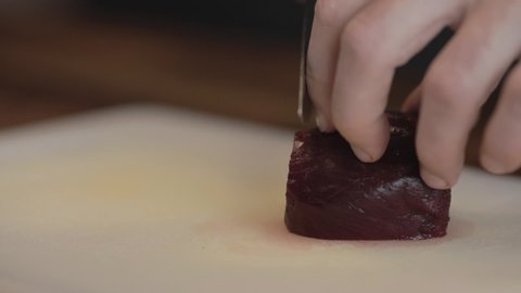Close-up view of hands thinly slicing and splaying a cooked beet on a wooden cutting board