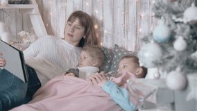 family watches attentively movie on bed with decorative gray pillows against wooden wall with LED fairy lights