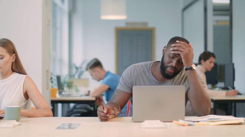 Young man reading bad news on laptop computer in office. Shocked african person taking off glasses in office. Afro man closing face with hands. | Shutterstock HD Video #1031832485