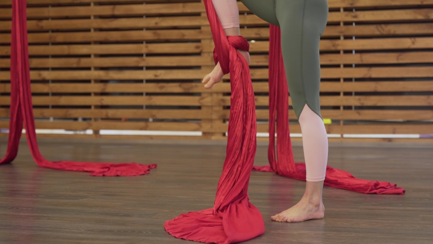 Fit girl dressed in tight leggins and pink top practising fly yoga-fitness. The sportsgirl rolling red hammock on her feet, moving up, lifting, doing upsidedown full-flip in the air, spinning around