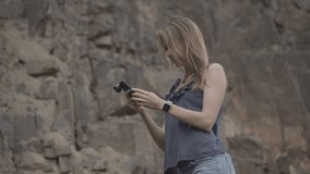 ProRes 4:2:2 log, slow motion, close up. Long haired pretty woman with casual clothes on making videos and photos on smartphone with auxiliary lens in basalt quarry. Seeing the results with interest