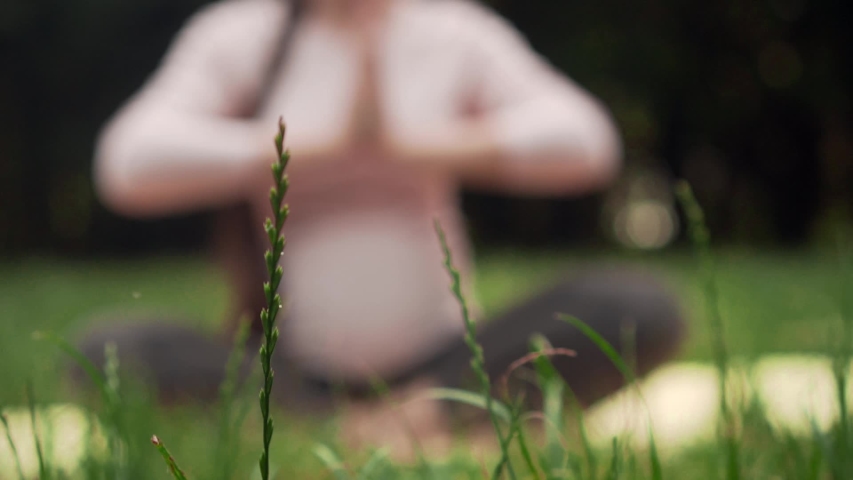 A pregnant woman practices yoga in the park sitting on a rug, sitting in the lotus position and meditates. Relaxing and being in a light lotus.