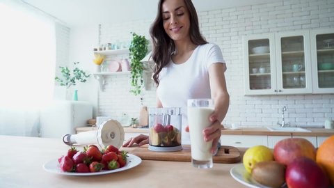 Healthy vegan smoothie with fruits. Beautiful happy young woman in casual home clothes is preparing fitness cocktail with vegetable milk and different season fruits on the kitchen at home. Sporty meal