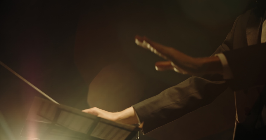 Close up shot of hands of symphony orchesra conductor directing music by waving his baton. Studio shot on black background 4k footage Royalty-Free Stock Footage #1031847851