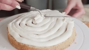 A close up video of icing smoothing process. the cook uses a shart palette knife in order to spread all the cream / icing over bottom part of the cake. She rolls white stand for making process easier