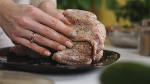 A woman rubs a whole chicken with salt and pepper before put it to bake in the oven.