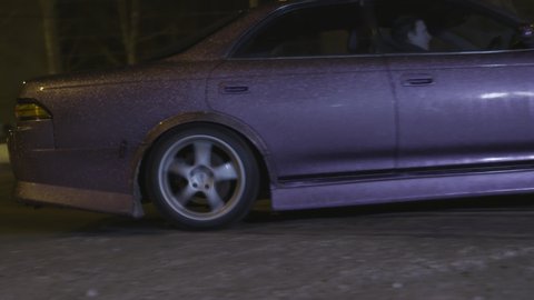 Beautiful purple passenger car drifting in the city streets at night in winter season. Action. A car going into a skid with dirt flying from under the wheels.