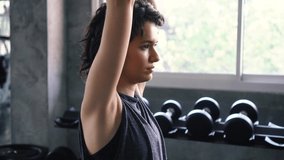 Young Caucasian fit woman doing overhead triceps extension exercise with dumbbell at the gym