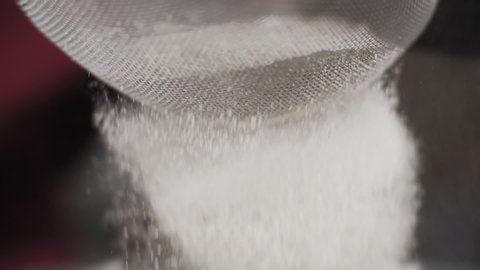 Close-up of flour through sieve fray. Sifting flour n slow motion. Baking. Ingredients and preparation stages. Sifting flour and a sieve in hands of chef.