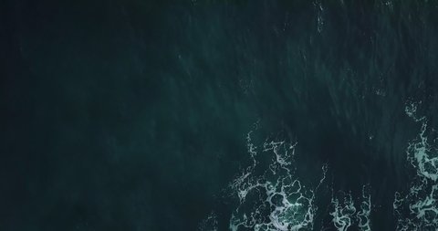 Timelapse. Aerial top view waves break on rocks in a blue ocean. Sea waves on beautiful beach aerial view drone 4k shot. Bird's eye view of ocean waves crashing against an empty stone from above.