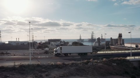 White Truck Drives Through Industrial Warehouse Area in Early Hours of the Morning . Follow-up Shot of a Semi-Truck with Cargo Trailer Moving on a Highway.