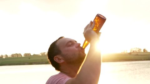 Drinking beer at sunset, Silhouette of a young man drinking beer out of a glass bottle at sunset